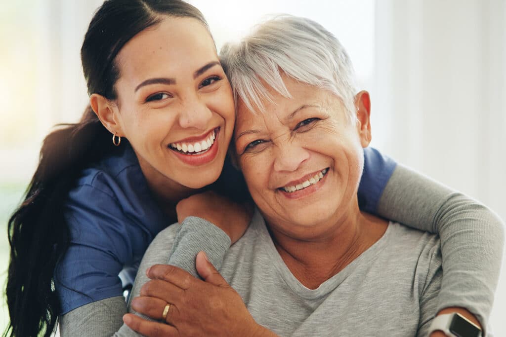Happy woman, nurse and hug senior patient in elderly care, support or trust at old age home. Portrait of mature female person, doctor or medical caregiver hugging with smile for embrace at house
